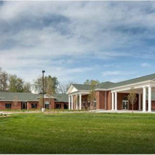 An exterior view of a brick institutional building with white columns and surrounding greenery.