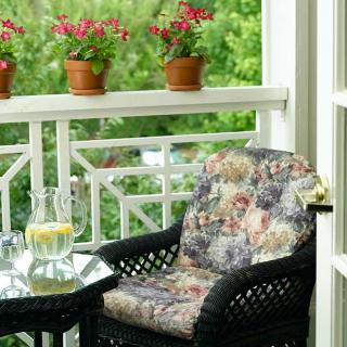 A cozy porch setup with a cushioned chair, table, and potted plants.