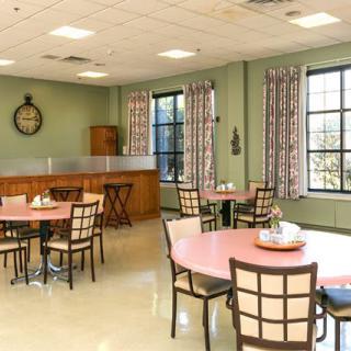 A well-lit dining area with multiple tables and chairs, featuring large windows and decorative curtains.