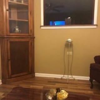 A cozy living room with a corner cabinet, window, and chair on wooden flooring.