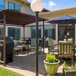 A cozy outdoor patio area with furniture, a grill, and potted plants under a clear blue sky.