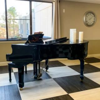 A grand piano placed in a room with a black and white checkered floor, accompanied by decorative candles and a wall-mounted clock.