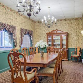 A traditional dining room with elegant wooden furniture, featuring a large dining table and chairs, chandeliers, and a china cabinet.