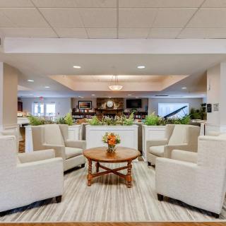A modern hotel lobby with a comfortable seating area, featuring cream-colored chairs and a round wooden table adorned with flowers.