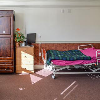 A neatly arranged hospital room with a bed, wardrobe, and small dresser.