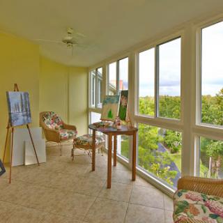 A bright and inviting sunroom featuring comfortable seating, art displays, and expansive windows offering a beautiful view of the outdoors.
