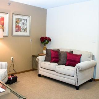 A cozy living room with neutral tones, featuring a comfortable sofa accented with red cushions and framed artwork on the walls.
