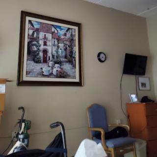 A view of a hospital room featuring a painting, furniture, and a clock.