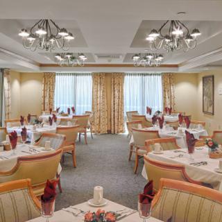 An elegant dining room with neatly arranged tables and chairs, adorned with white tablecloths and decorative chandeliers.