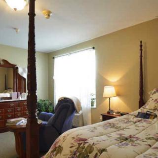 A cozy bedroom featuring a four-poster bed, a wooden dresser with a mirror, an armchair, and a bedside lamp.