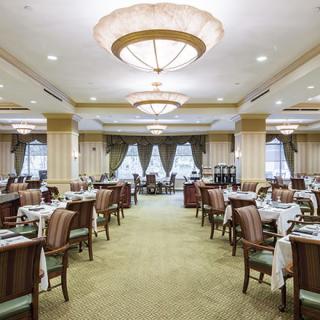 An elegant dining room with neatly arranged tables and chairs, illuminated by large chandeliers.