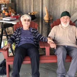 An elderly couple sits on a bench, holding hands and relaxing on the patio.