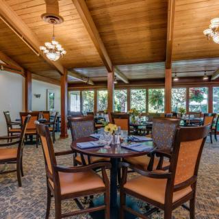 A cozy dining area with wooden ceilings and elegantly set tables, bathed in natural light from large windows.