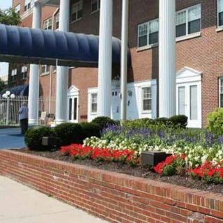 A building entrance with columns, landscaped flowers, and a brick pathway.