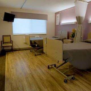 A modern patient room in a hospital, featuring a bed, chair, and large window.