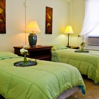 A cozy bedroom with twin beds featuring green bedding, illuminated by warm lamps and accented with floral decor.