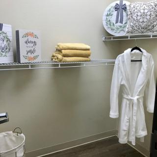A neatly organized closet with a white robe, yellow towels, and decorative items on shelves.