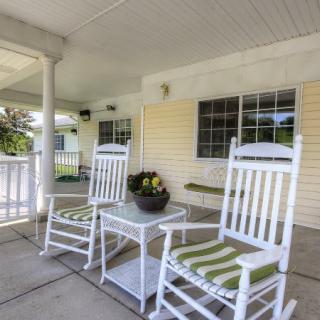 A cozy porch with white rocking chairs and a small table with flowers, perfect for relaxing on a summer day.