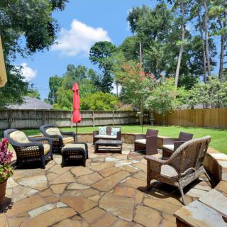 A cozy backyard patio with comfortable seating and a vibrant umbrella, surrounded by greenery.