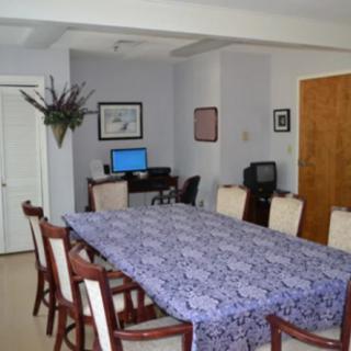 A dining room or meeting area with a large table and chairs, featuring a computer and television for presentations.