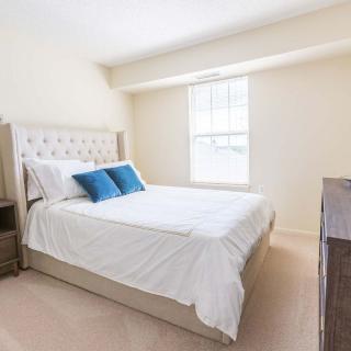 A bright and simple bedroom with a neatly made bed, two blue pillows, and a window bringing in natural light.