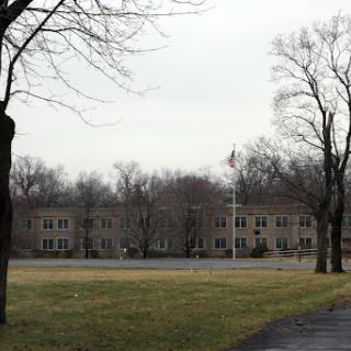 A view of a building surrounded by bare trees and an open grassy area under an overcast sky.