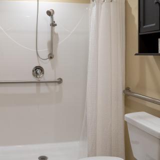 A bathroom with a bathtub, shower setup, and safety grab bars.