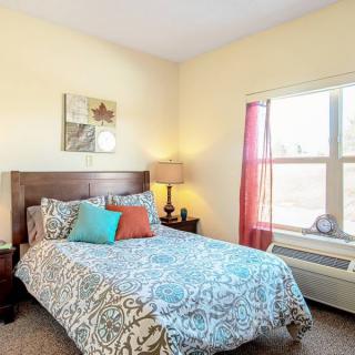 A cozy bedroom with a neatly made bed and colorful pillows, featuring a window allowing natural light to brighten the space.