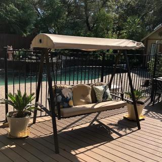 A patio swing with a canopy set on a wooden deck, surrounded by potted plants.