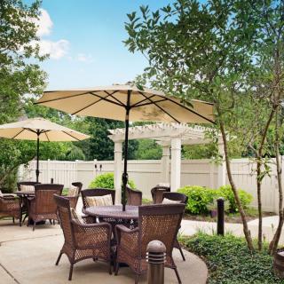A tranquil outdoor patio area with wicker furniture and large umbrellas surrounded by greenery.