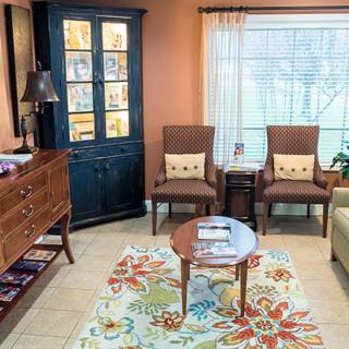 A cozy living room with colorful decor, featuring chairs, a cabinet, and a floral rug.