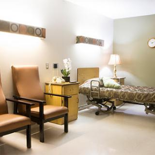 A serene hospital patient room featuring a bed, two chairs, and a bedside lamp, designed for comfort and care.