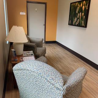 A cozy waiting area featuring comfortable chairs, a lamp, and wall art.