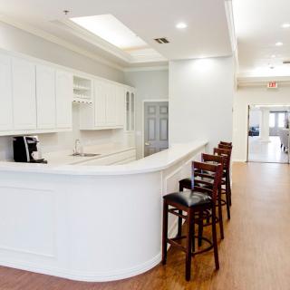 A modern kitchen interior featuring a white counter with bar stools, white cabinets, and wooden flooring.