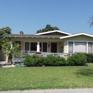 A suburban house with a neatly maintained lawn and greenery under a clear blue sky.