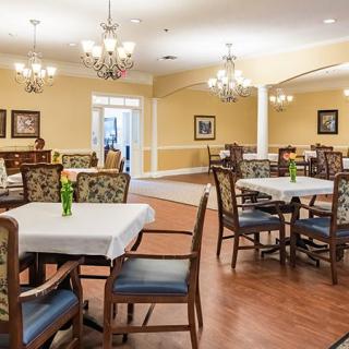 A well-decorated dining room with multiple tables and chairs, featuring chandeliers and a wooden floor.