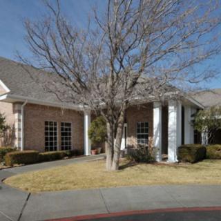 A brick house with white columns and a tree in the front yard.