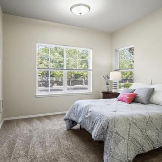 A cozy bedroom with a large window, featuring a neatly made bed and bedside lamp.