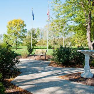 A serene park pathway lined with trees, featuring a bench and a birdbath.
