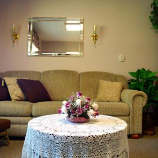 A cozy living room setup featuring a comfortable sofa, decorative table with flowers, and a mirror on the wall.