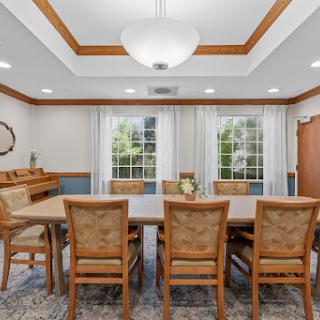 A well-lit dining room featuring a wooden table surrounded by upholstered chairs, complemented by natural light from large windows.