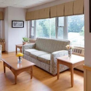 A cozy living room featuring a sofa, wooden coffee tables, and large windows providing natural light.