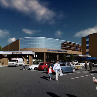 A modern hospital entrance showcasing contemporary architecture with visitors and vehicles in the parking area.