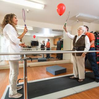 An elderly patient participates in a rehabilitation exercise with the help of healthcare professionals, using balloons to enhance coordination.