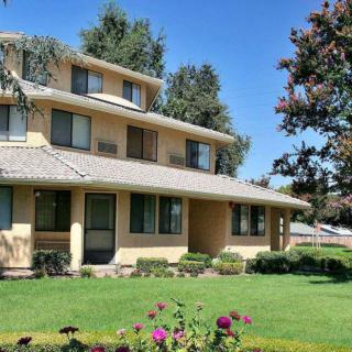 A large suburban house with a well-maintained lawn and trees under a clear blue sky.
