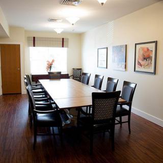 A spacious conference room with a long table and several chairs, featuring artwork on the walls and a wooden floor.