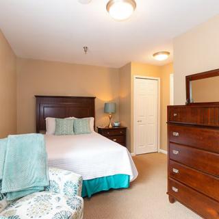 A cozy bedroom with a bed, dresser, and a lamp in a warmly lit room.