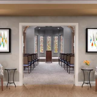 A serene chapel interior featuring rows of chairs, a central podium, and colorful artwork on the walls.