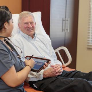 A nurse interacts with an elderly patient while using a tablet in a healthcare setting.