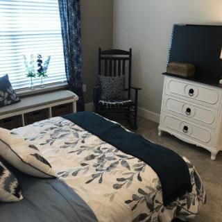 A cozy bedroom with a floral bedspread, a white dresser, and a rocking chair by the window.